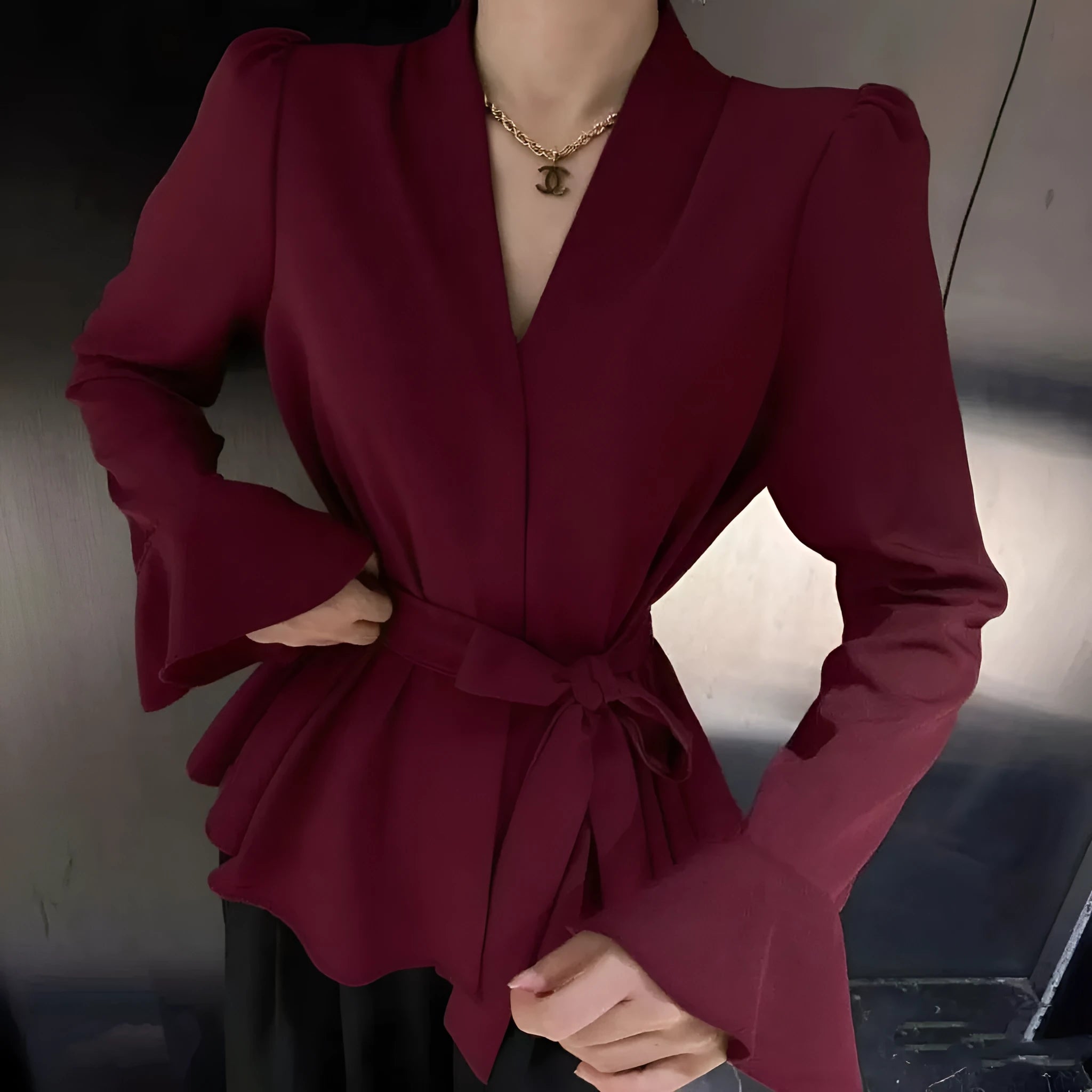 Woman wearing a wine red long sleeve shirt with an irregular French collar, bell sleeves, and a tie front.
