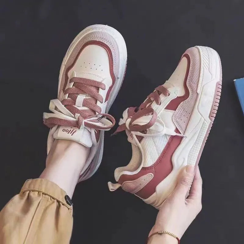 Pink and beige low top women's sneakers with a rubber sole on a neutral background.
