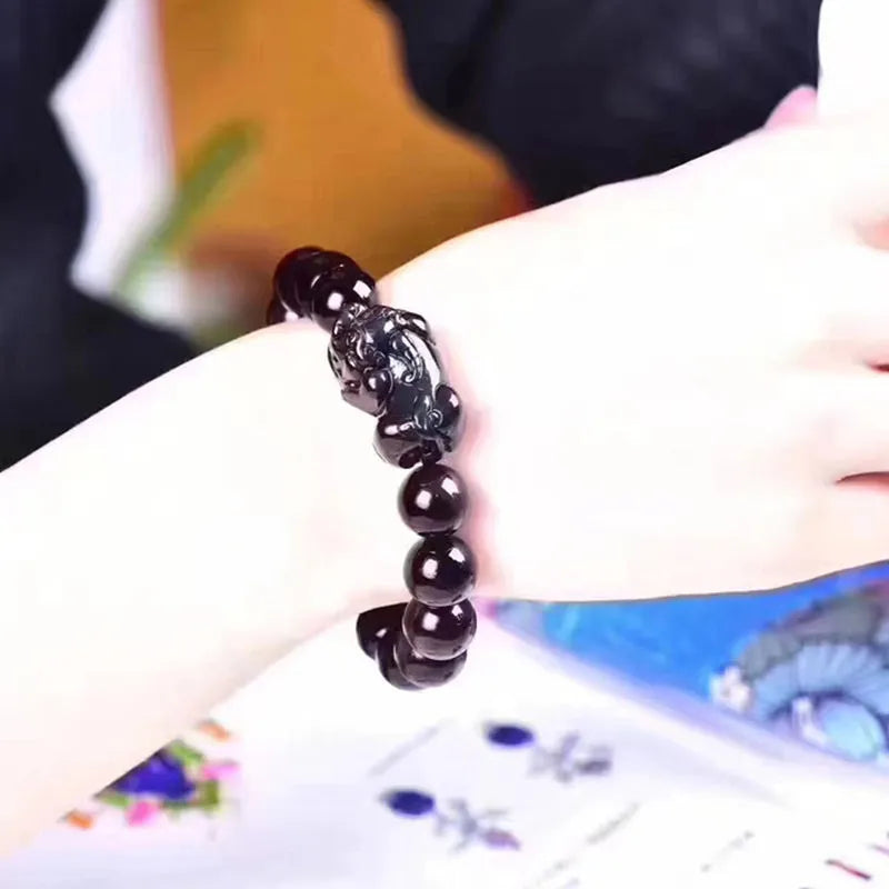 Natural obsidian stone bead bracelet with adjustable black cord on a wrist.