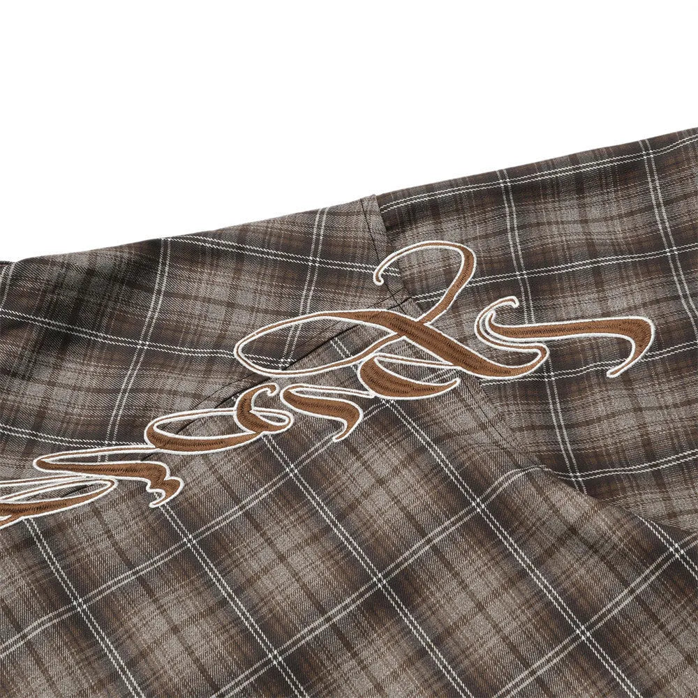 Man wearing a black and brown plaid short sleeve shirt with embroidered letters on the lapel
