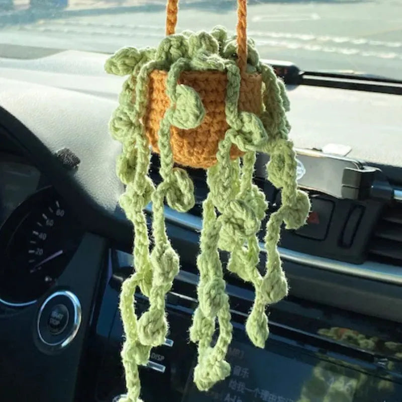 Green and white knitted wool car plant decoration with hanging rope on car dashboard
