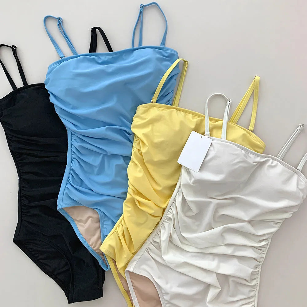 Sling style one-piece swimsuit with belly pleating in a solid colour.