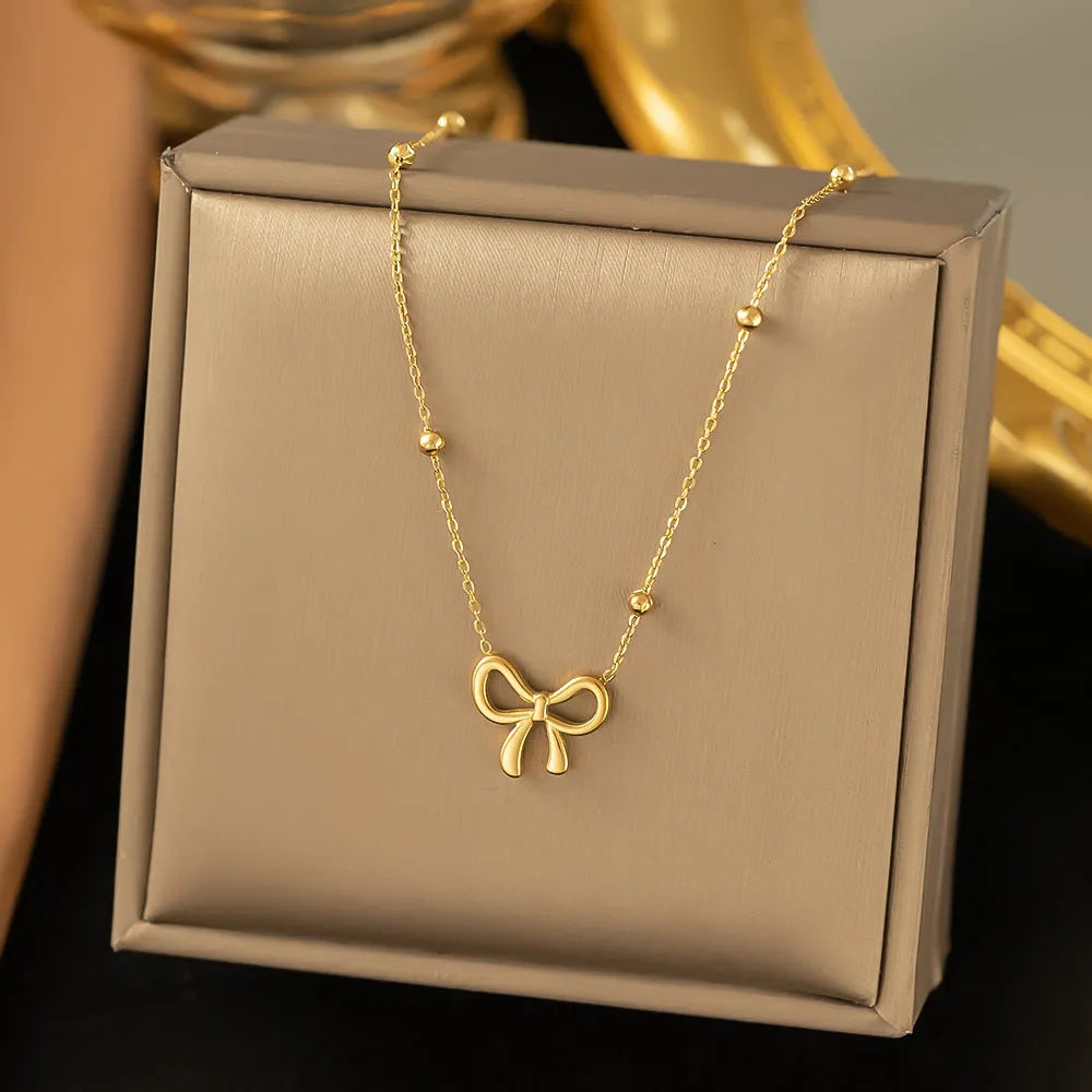 Gold electroplated bow necklace with adjustable chain on dark background