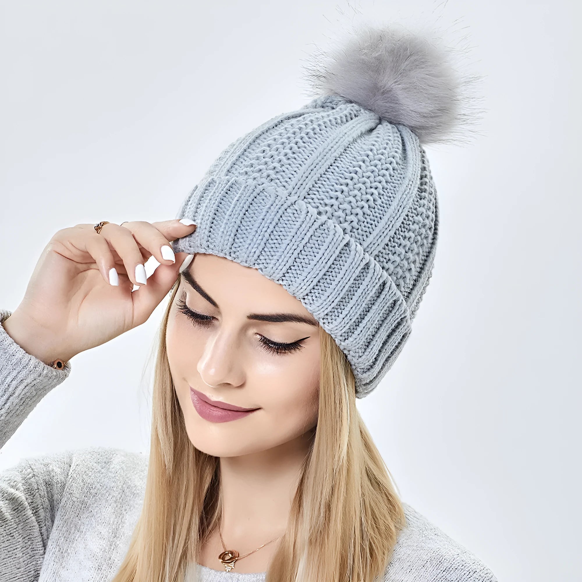 Woman wearing a light grey wool beanie with a faux fur pom pom and satin lining.
