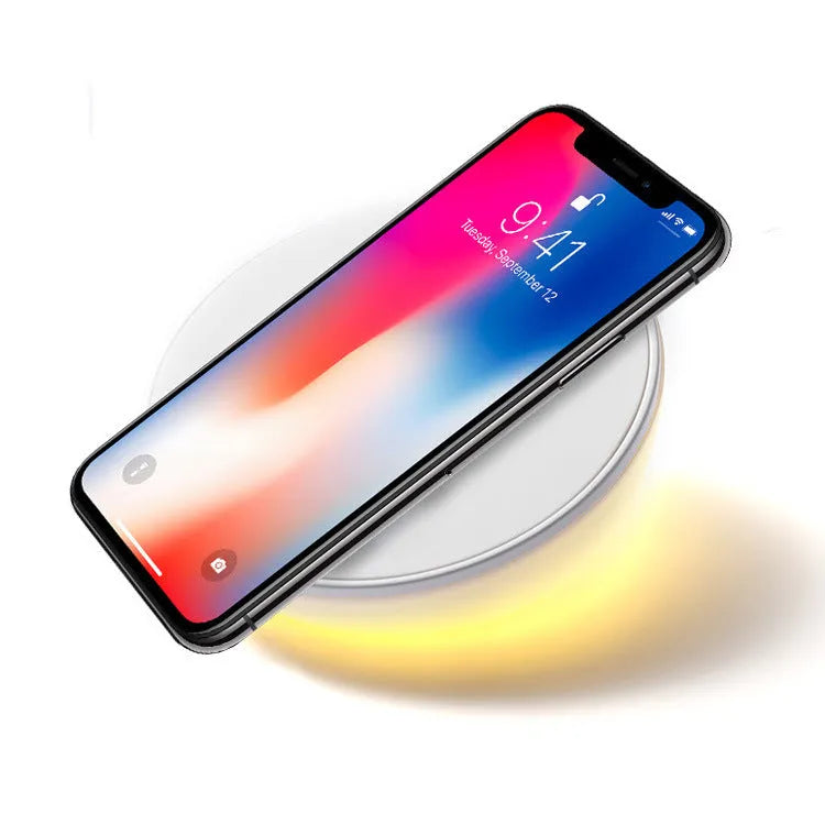 White Qi wireless charger with digital clock display on a desk next to a mobile phone.
