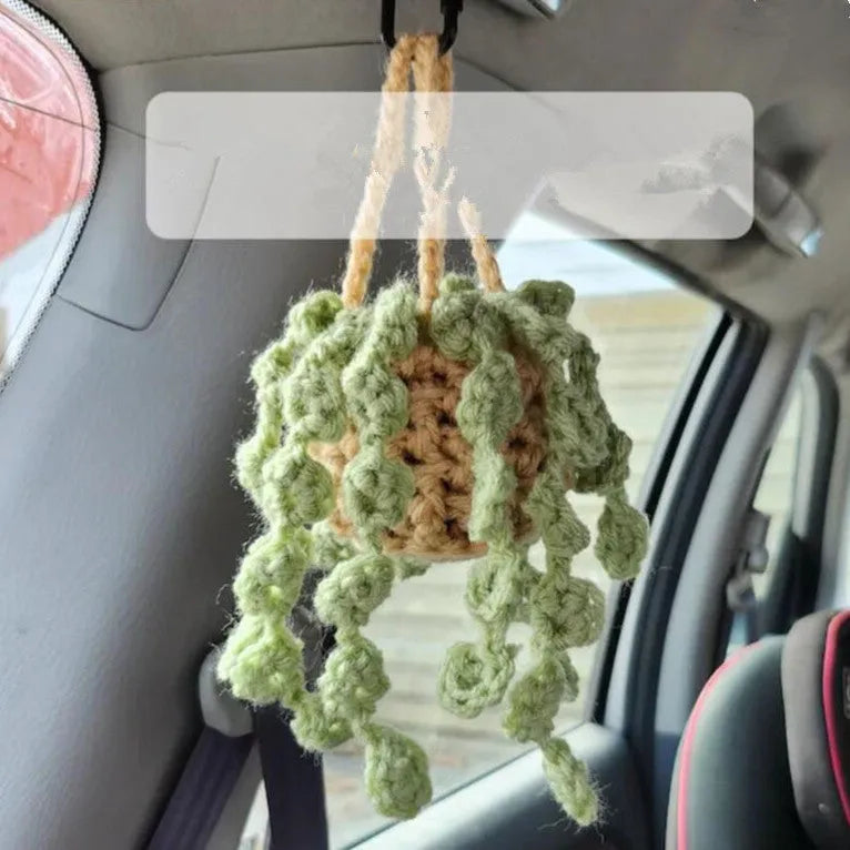 Green and white knitted wool car plant decoration with hanging rope on car dashboard