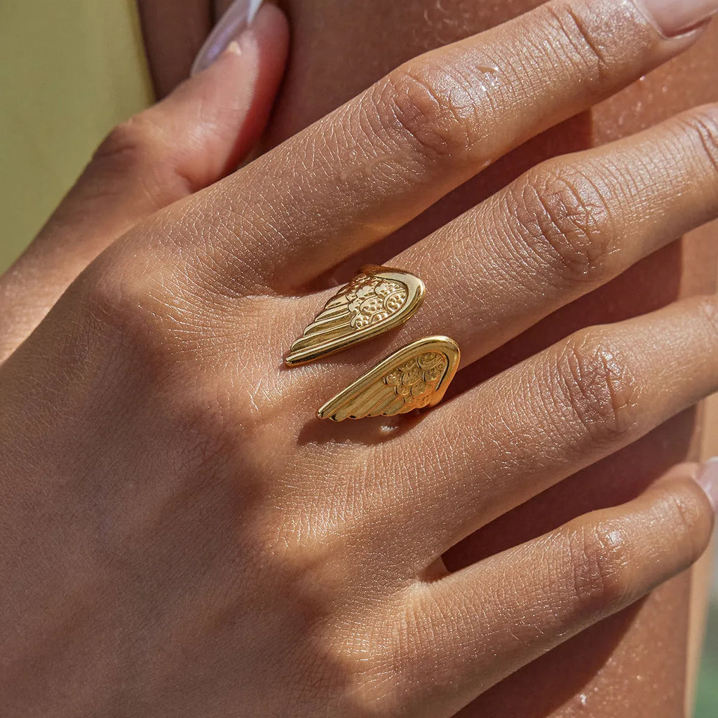 Stainless steel wings ring with open front design and electroplated metallic finish.