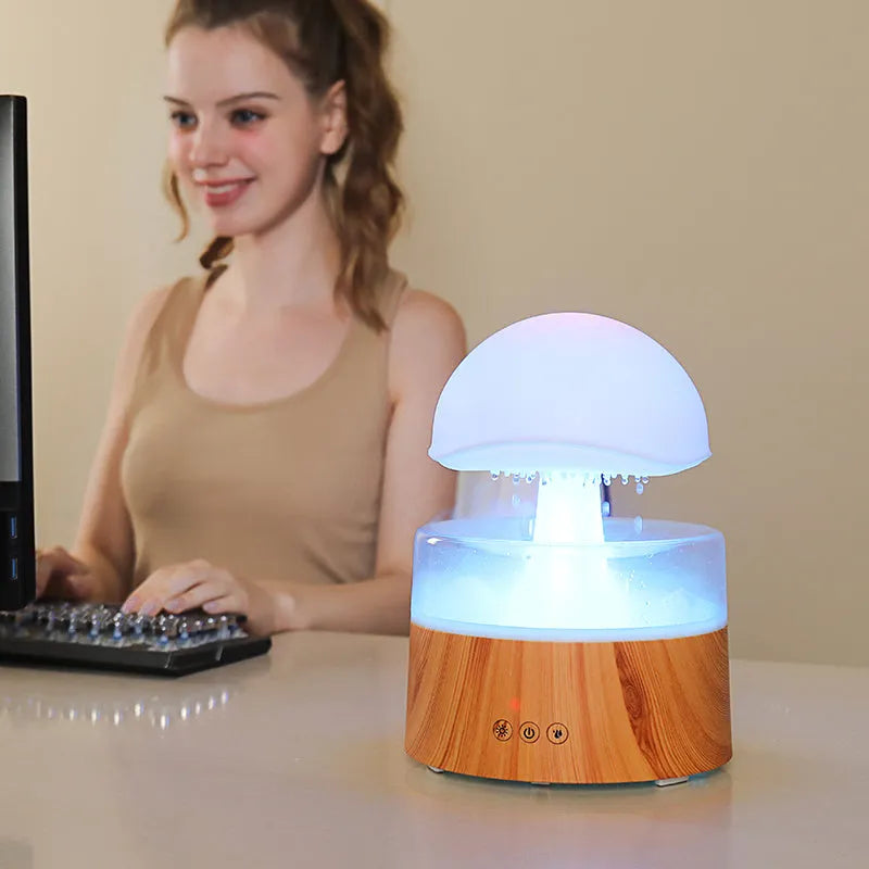 White cloud-shaped humidifier diffuser with LED rain effect and remote control on a wooden table.