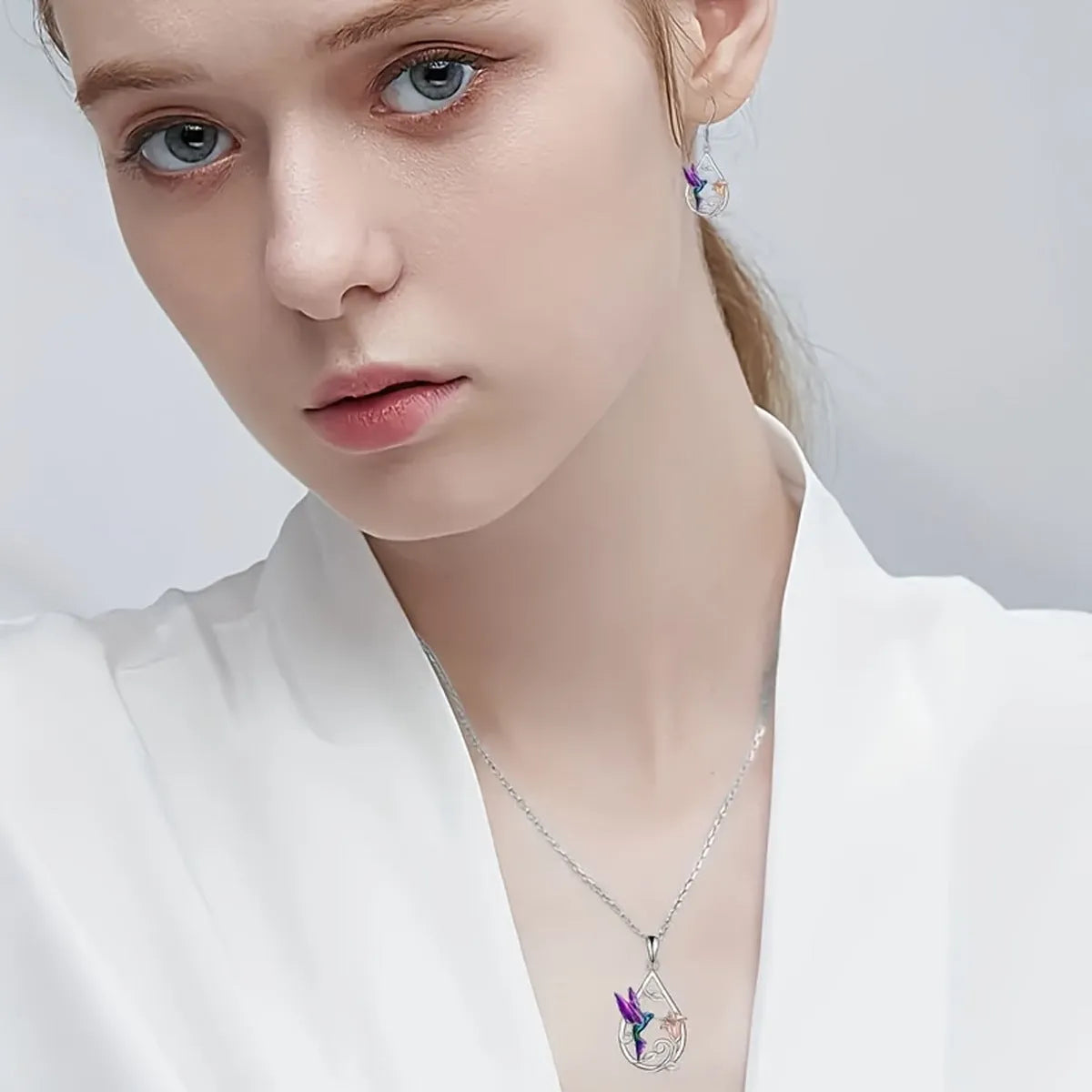 White electroplated copper hummingbird necklace and earring set with animal motifs on a neutral background