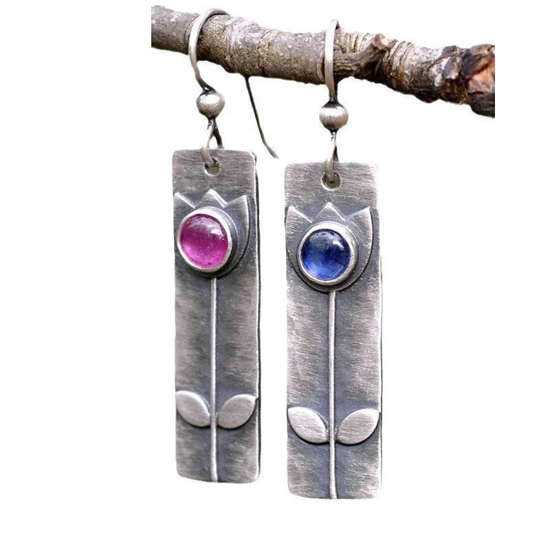 A pair of antique finish red sapphire earrings with a geometric shape and oval details on a white background.