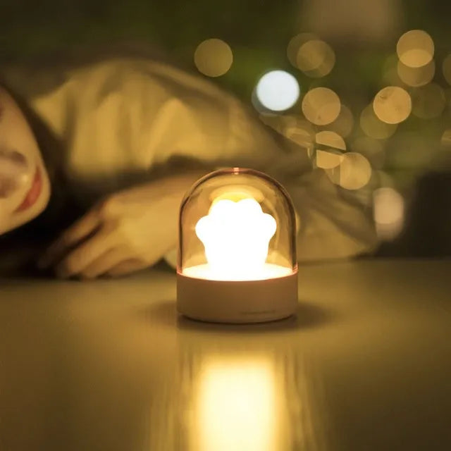 Grey or pink cat paw shaped USB rechargeable night light with music box function on a desk.