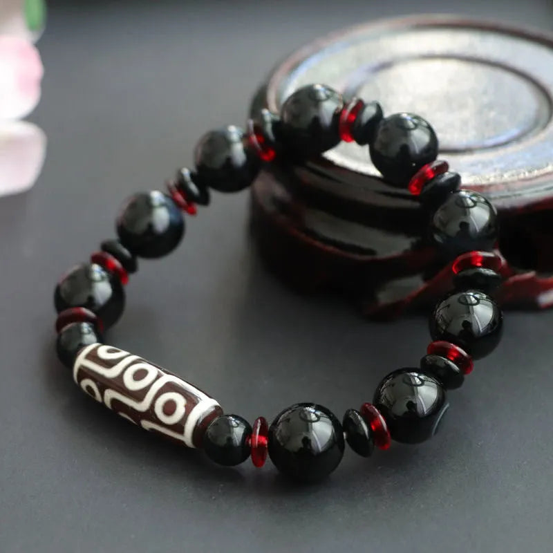 Close-up of a hand-woven black agate bracelet with 11mm geometric beads featuring traditional dzi patterns.