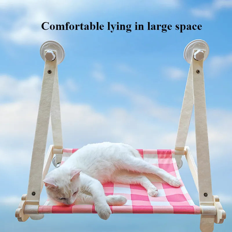 Pink wooden cat hammock with suction cups attached to a window, showing a cat resting on the linen fabric.