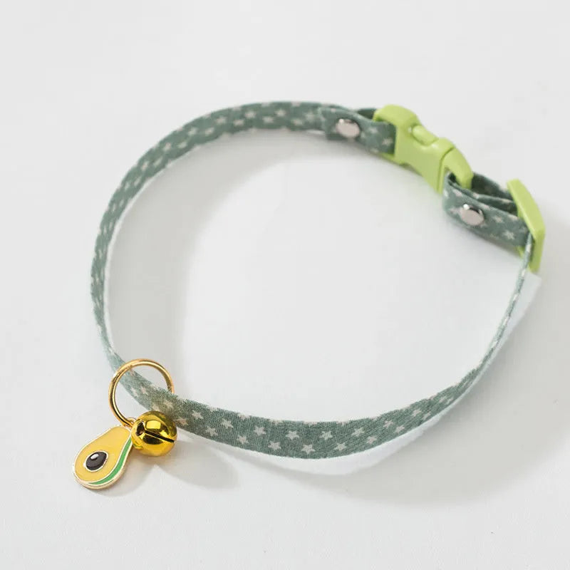 Green adjustable cat collar with a metal bell and a pink bow tie attached, shown on a measuring tape indicating size