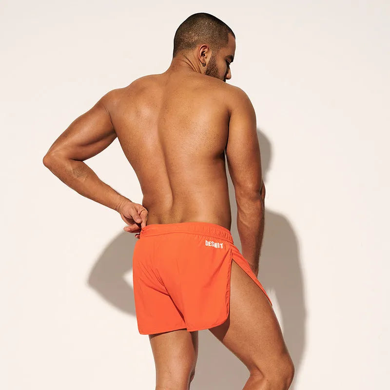 Man wearing loose orange red polyester shorts on a beach, demonstrating the micro-elastic fit.