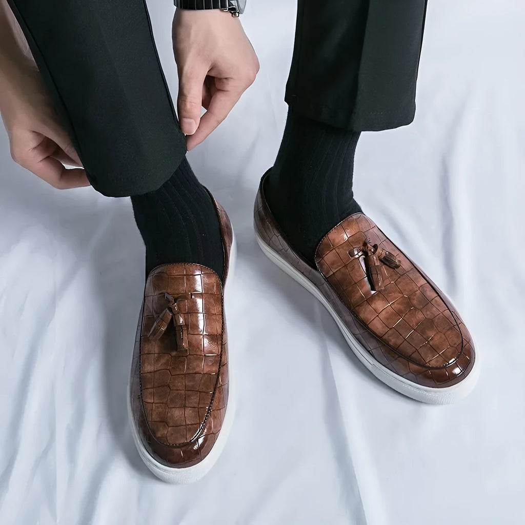 Men's black tassel detail slip-on sneakers on a white background, showing the round toe and elastic side.