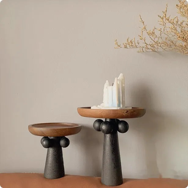 Round natural wooden tray with high legs holding a candle and perfume bottle on a table.