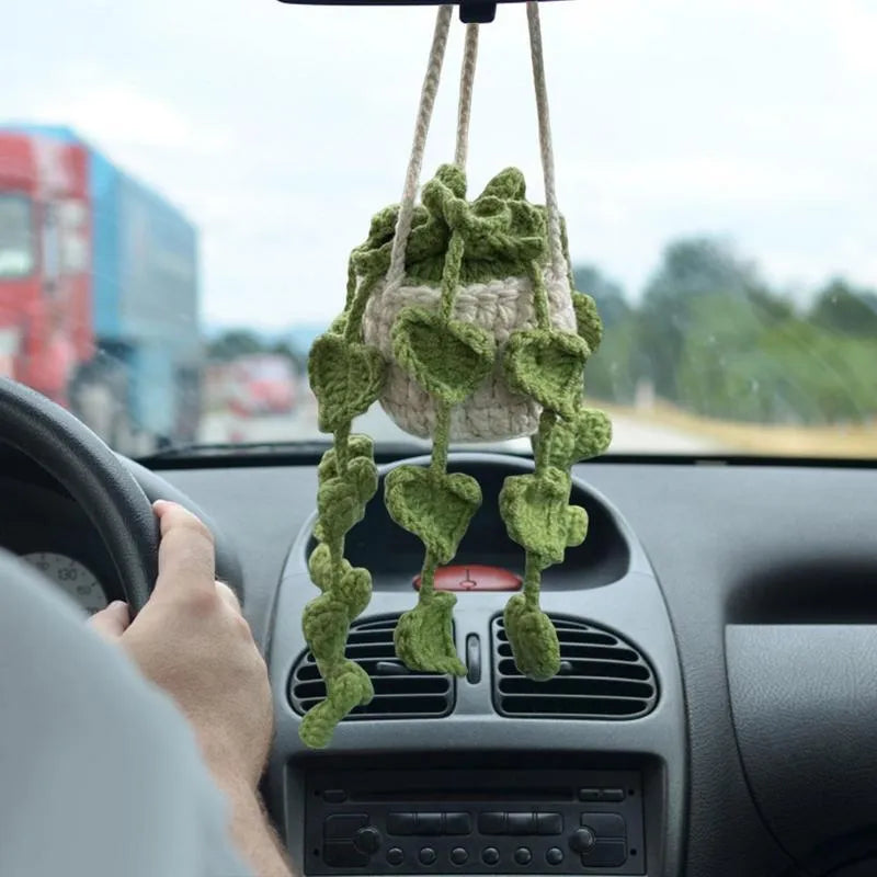 Green and white knitted wool car plant decoration with hanging rope on car dashboard