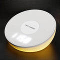 White Qi wireless charger with digital clock display on a desk next to a mobile phone.