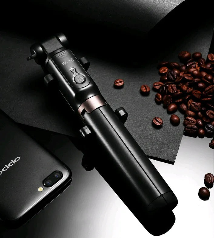Aluminium Bluetooth selfie stick with tripod base and remote control next to a mobile phone.