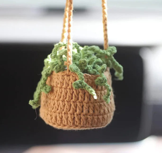 Green and white knitted wool car plant decoration with hanging rope on car dashboard