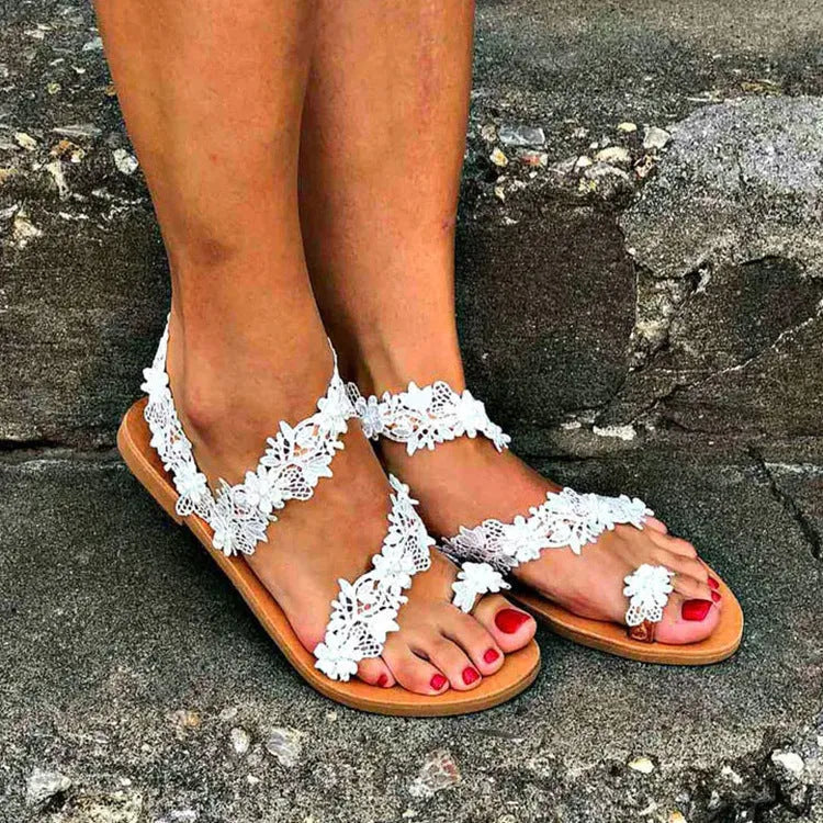 White women's flat sandals with rhinestone flower decoration on PU upper and rubber sole.