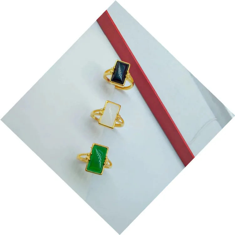 Adjustable brass gold-plated ring with a central green artificial gemstone on a finger.
