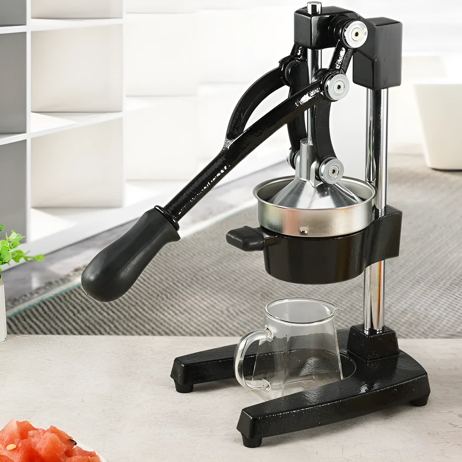 A black cast iron manual citrus juicer with a stainless steel strainer on a kitchen counter.