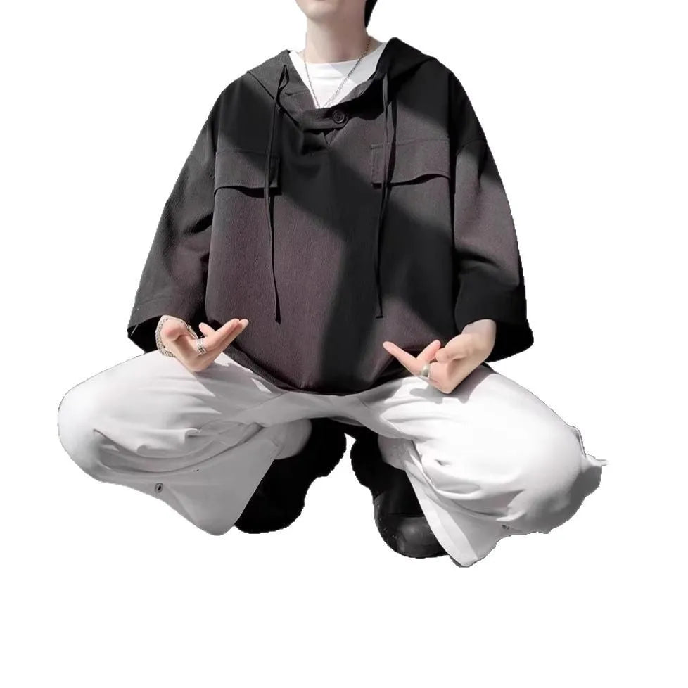 Man modelling a loose grey hooded short sleeve t-shirt, showing the pullover style and front design.
