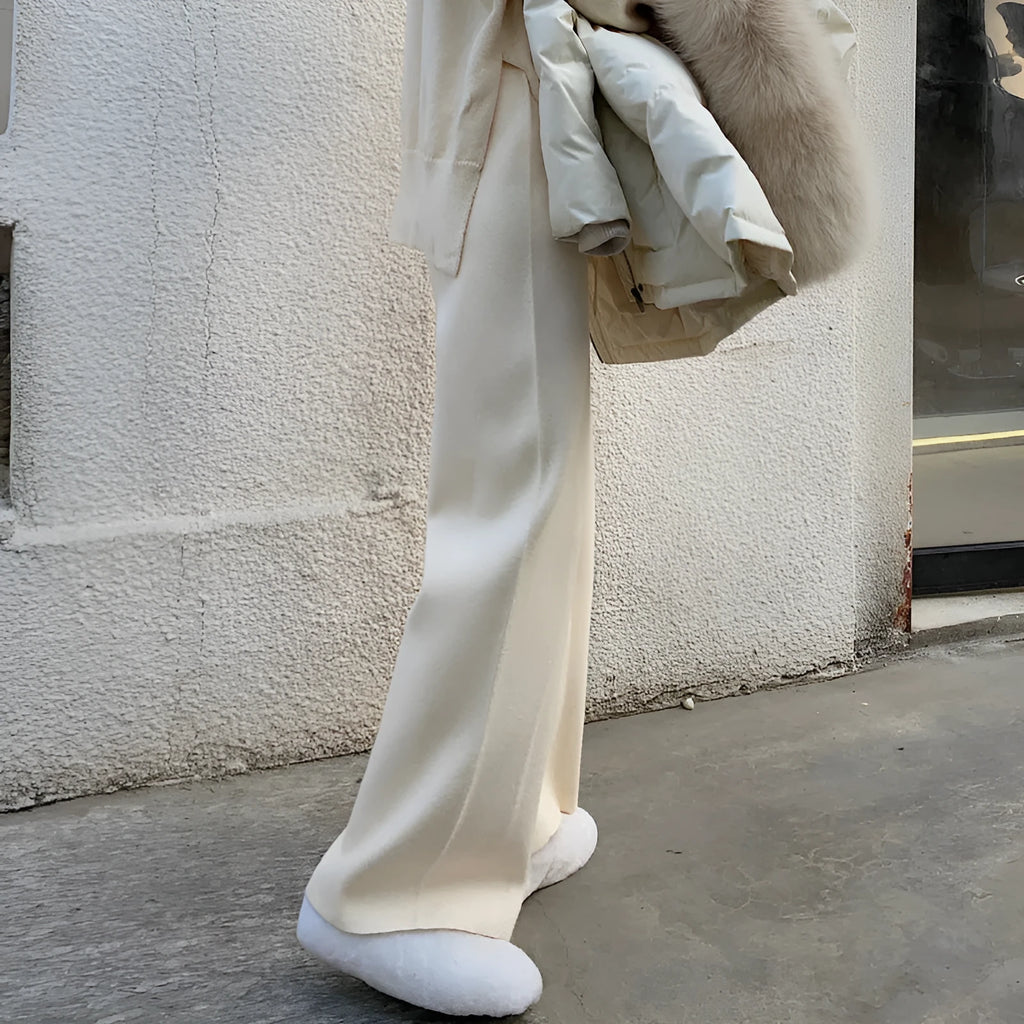 Woman wearing high waist cream white knitted wide-leg trousers with a straight, drooping mopping cut.