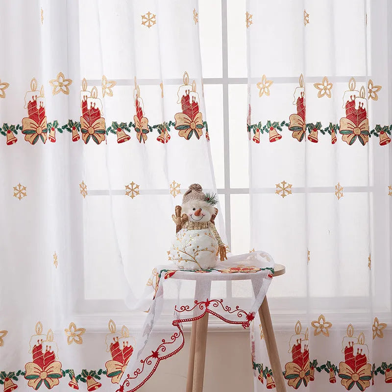 Pair of white Christmas curtains with embroidered red and green snowflake design, hung on a window.