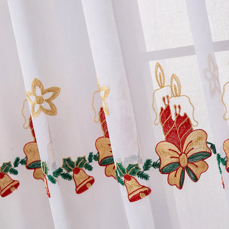 Pair of white Christmas curtains with embroidered red and green snowflake design, hung on a window.