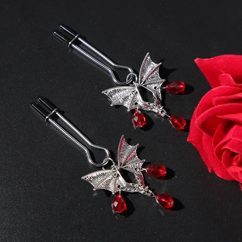 Silver bat-shaped nipple clamp with ruby gemstone and adjustable mechanism.