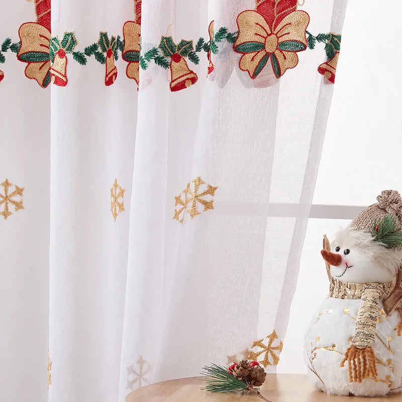 Pair of white Christmas curtains with embroidered red and green snowflake design, hung on a window.