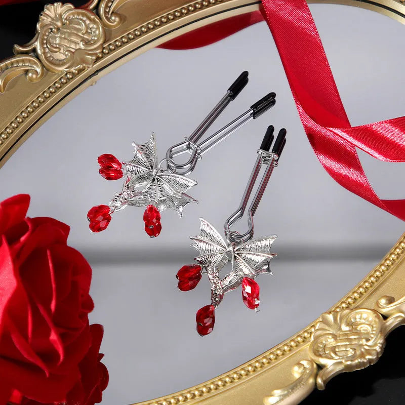 Silver bat-shaped nipple clamp with ruby gemstone and adjustable mechanism.