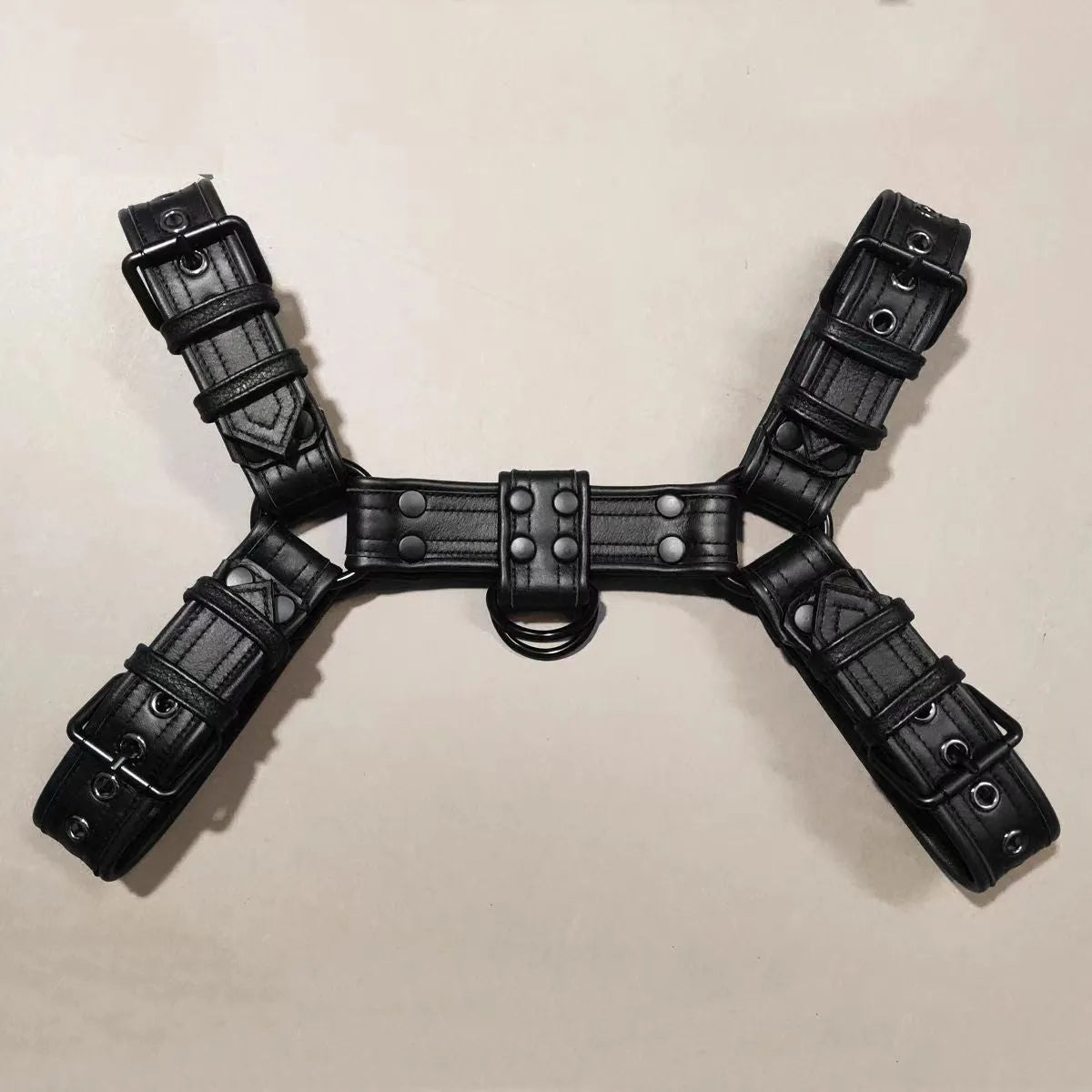 Black leather chest harness strap with a metal buckle and rivets on a neutral background.