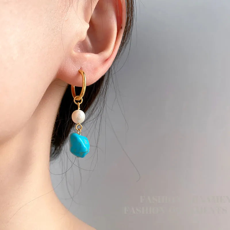 A pair of women's geometric drop earrings with irregular turquoise stones and round cultured pearls on copper settings.
