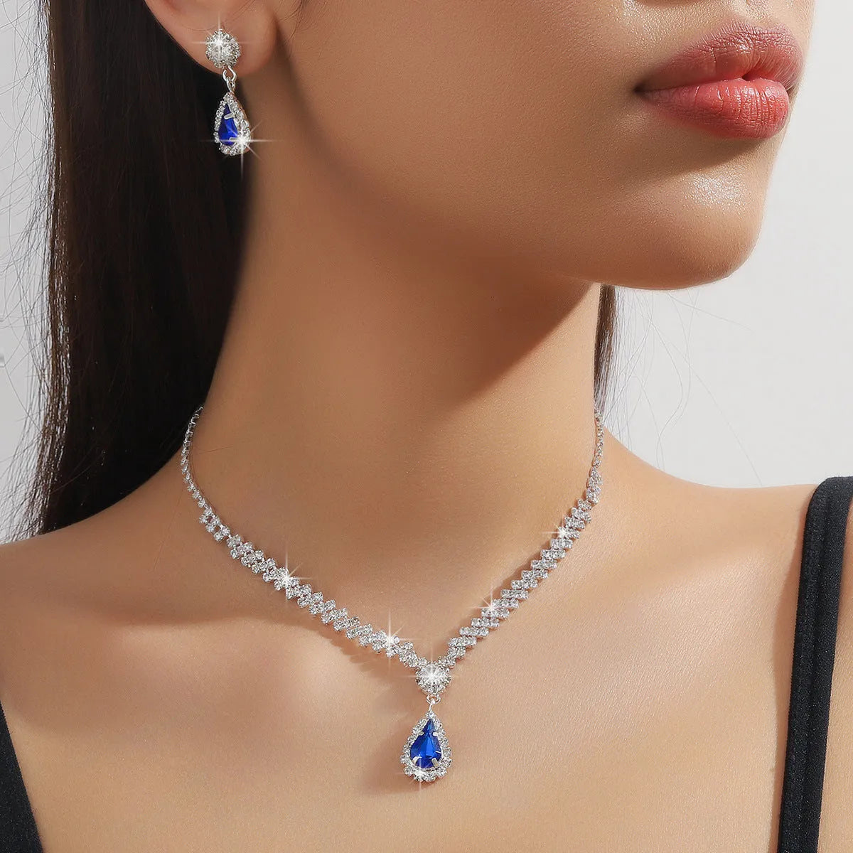 Women's blue claw chain necklace and drop rhinestone earrings from a matching jewellery set.