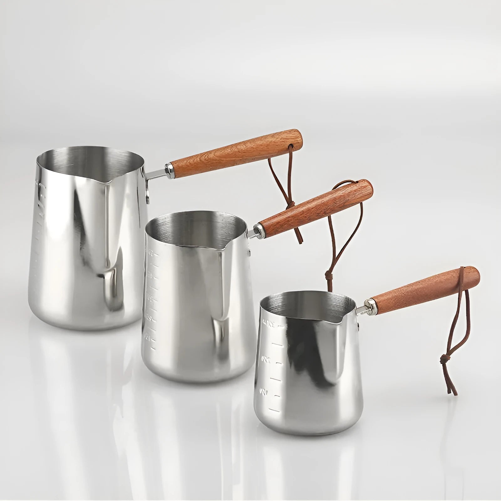Stainless steel milk frothing jug with volume scale and wooden handle in three size options.