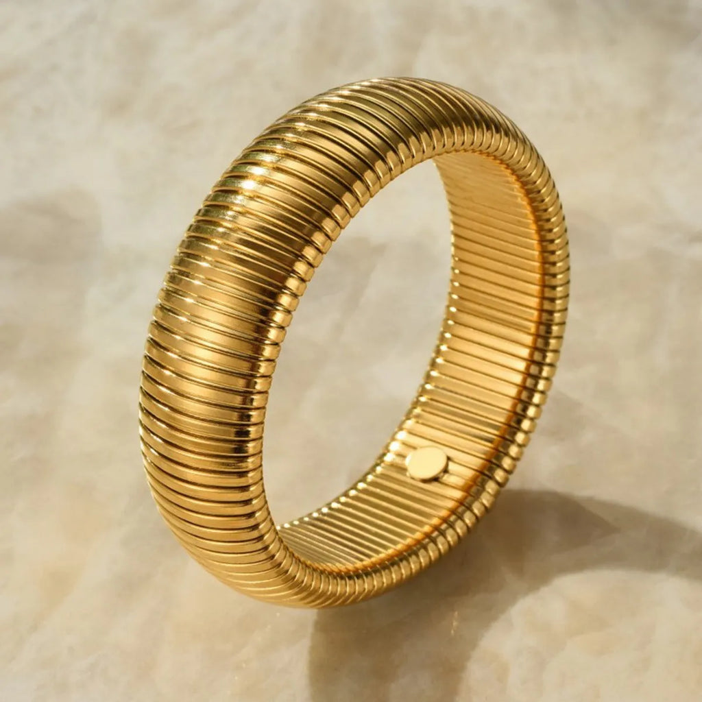 Close-up of a women's elastic titanium steel bracelet featuring a bold vertical stripe ring pattern in a gold tone finish.