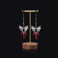 Silver bat-shaped nipple clamp with ruby gemstone and adjustable mechanism.