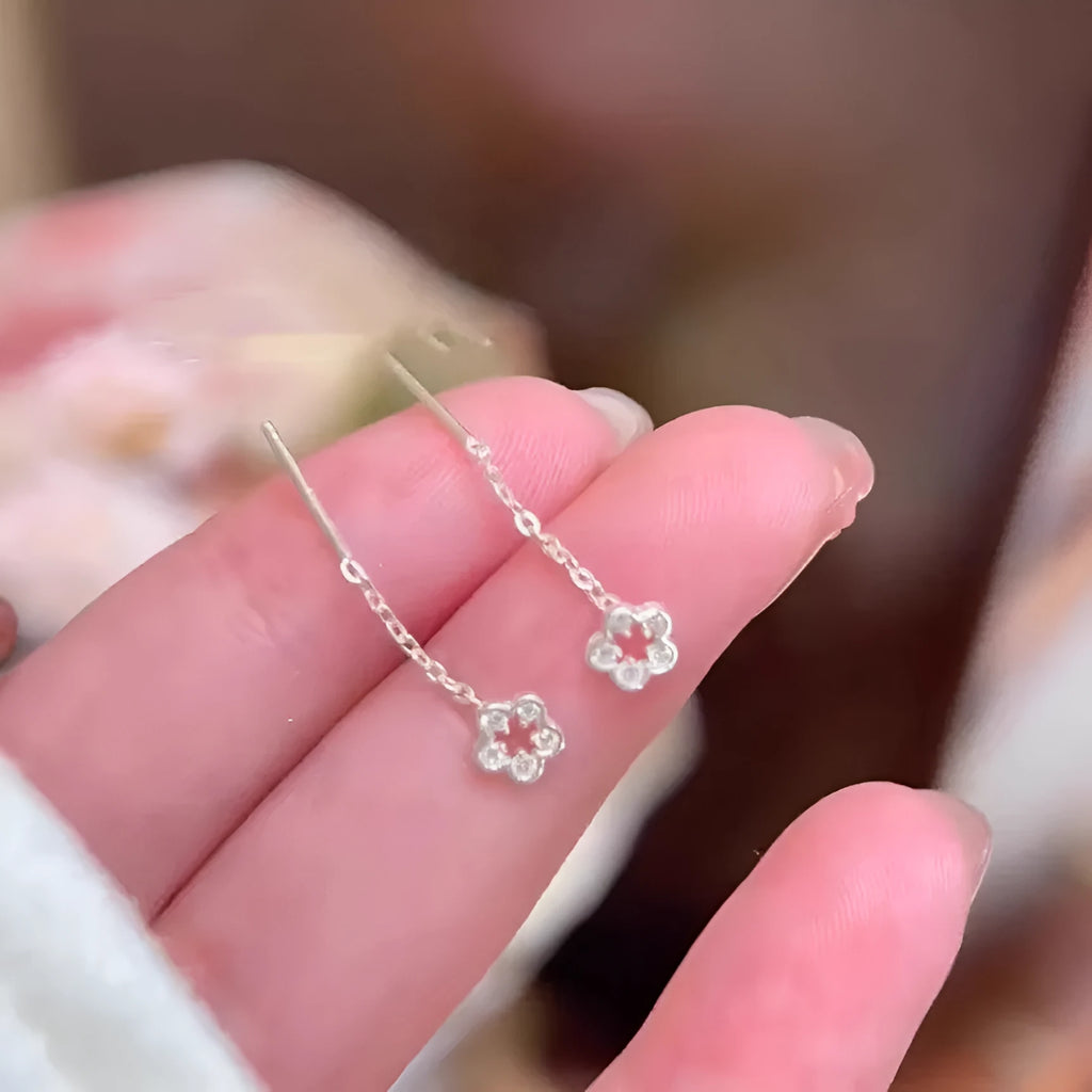 A pair of silver-coloured hollow flower drop earrings with detailed petals, shown against a plain background.