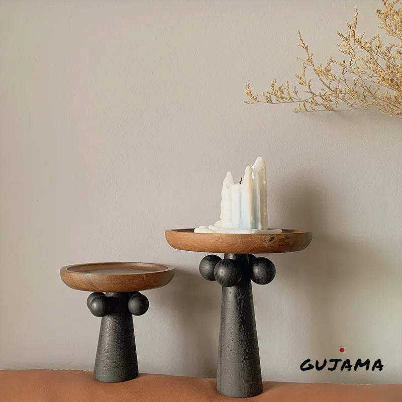 Round natural wooden tray with high legs holding a candle and perfume bottle on a table.