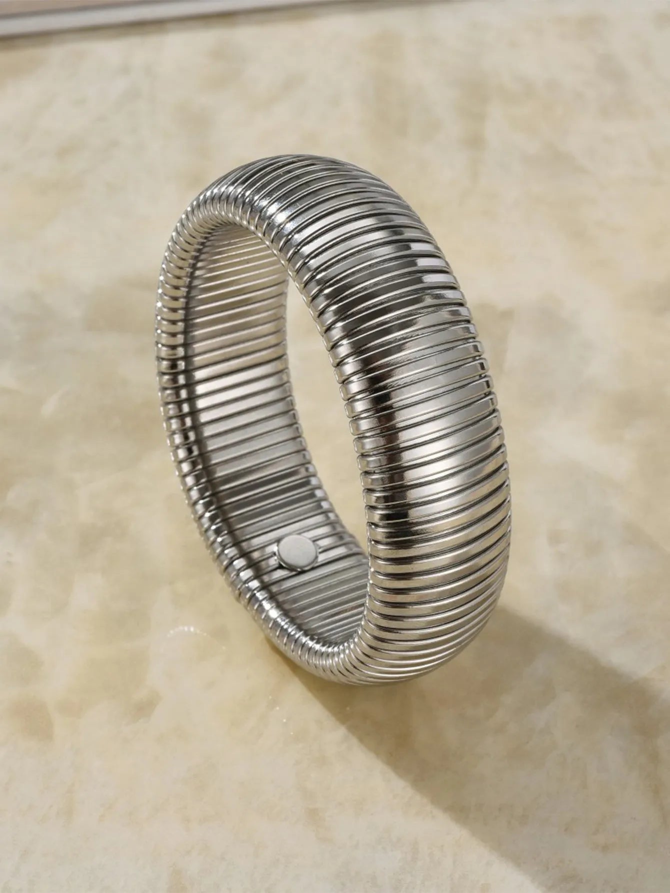 Close-up of a women's elastic titanium steel bracelet featuring a bold vertical stripe ring pattern in a gold tone finish.
