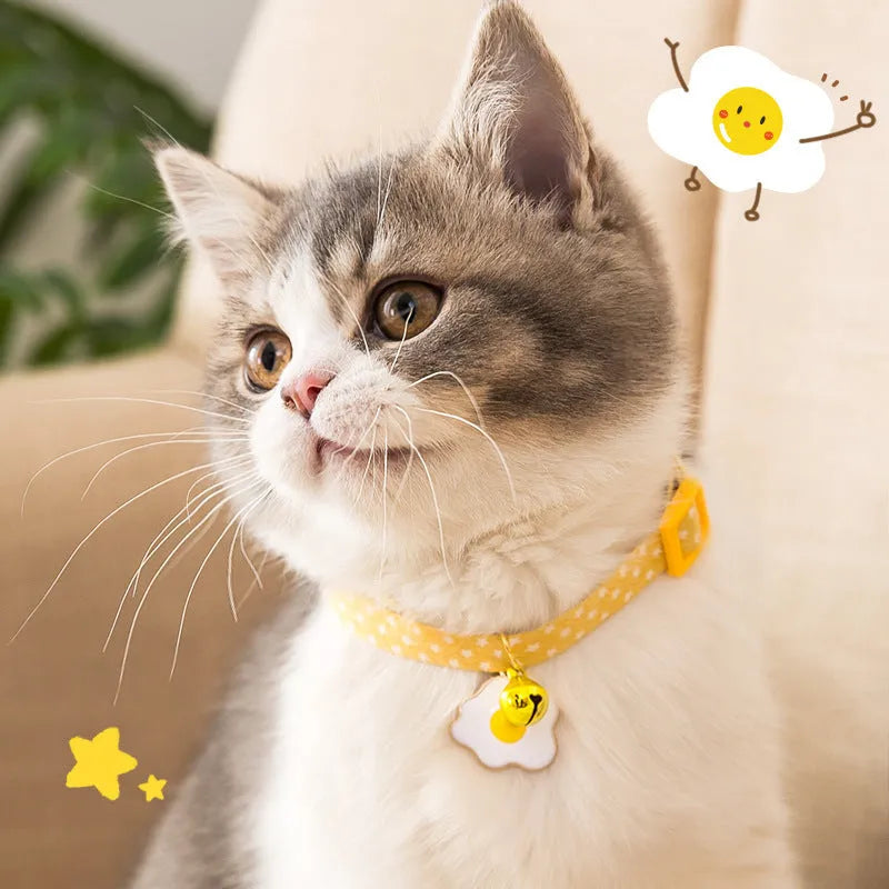 Green adjustable cat collar with a metal bell and a pink bow tie attached, shown on a measuring tape indicating size