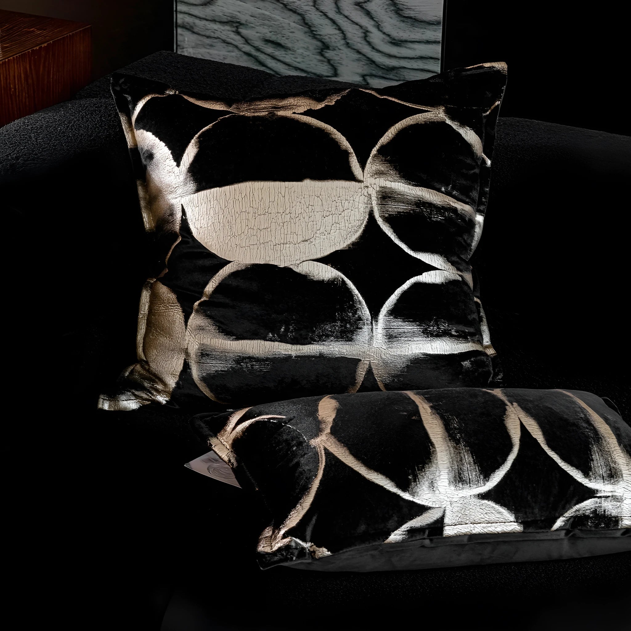 Black and gold abstract patterned flannel cushion in square and bolster sizes on a grey sofa.