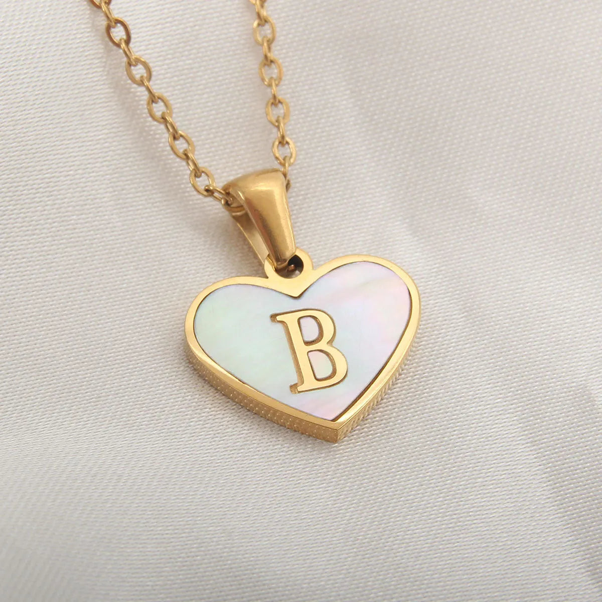 Gold-plated heart necklace with white shell pendant personalised with a letter, on an adjustable chain.