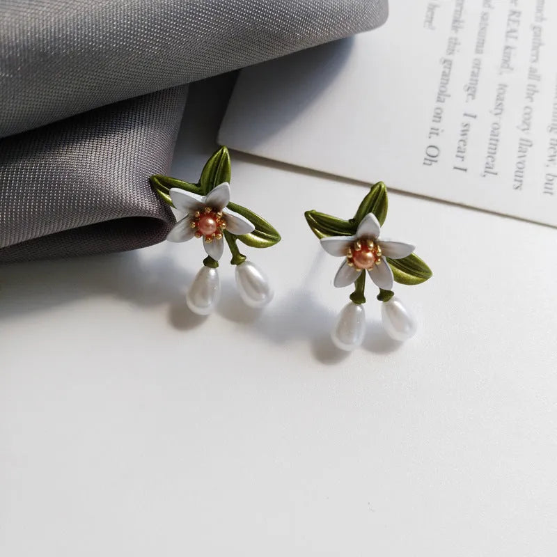 A pair of women's earrings showing sterling silver camellia flower studs and a matching alloy flower clip on a white background.
