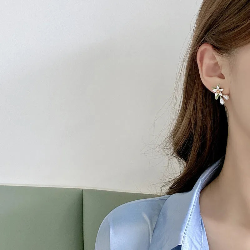 A pair of women's earrings showing sterling silver camellia flower studs and a matching alloy flower clip on a white background.
