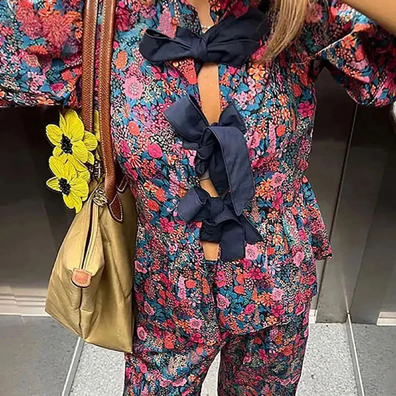 Floral print two-piece leisure suit with tie-neck blouse, puff sleeves, and long trousers.